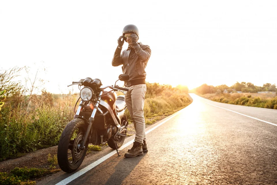 Motociclista ao lado de sua moto em uma estrada ao pôr do sol
